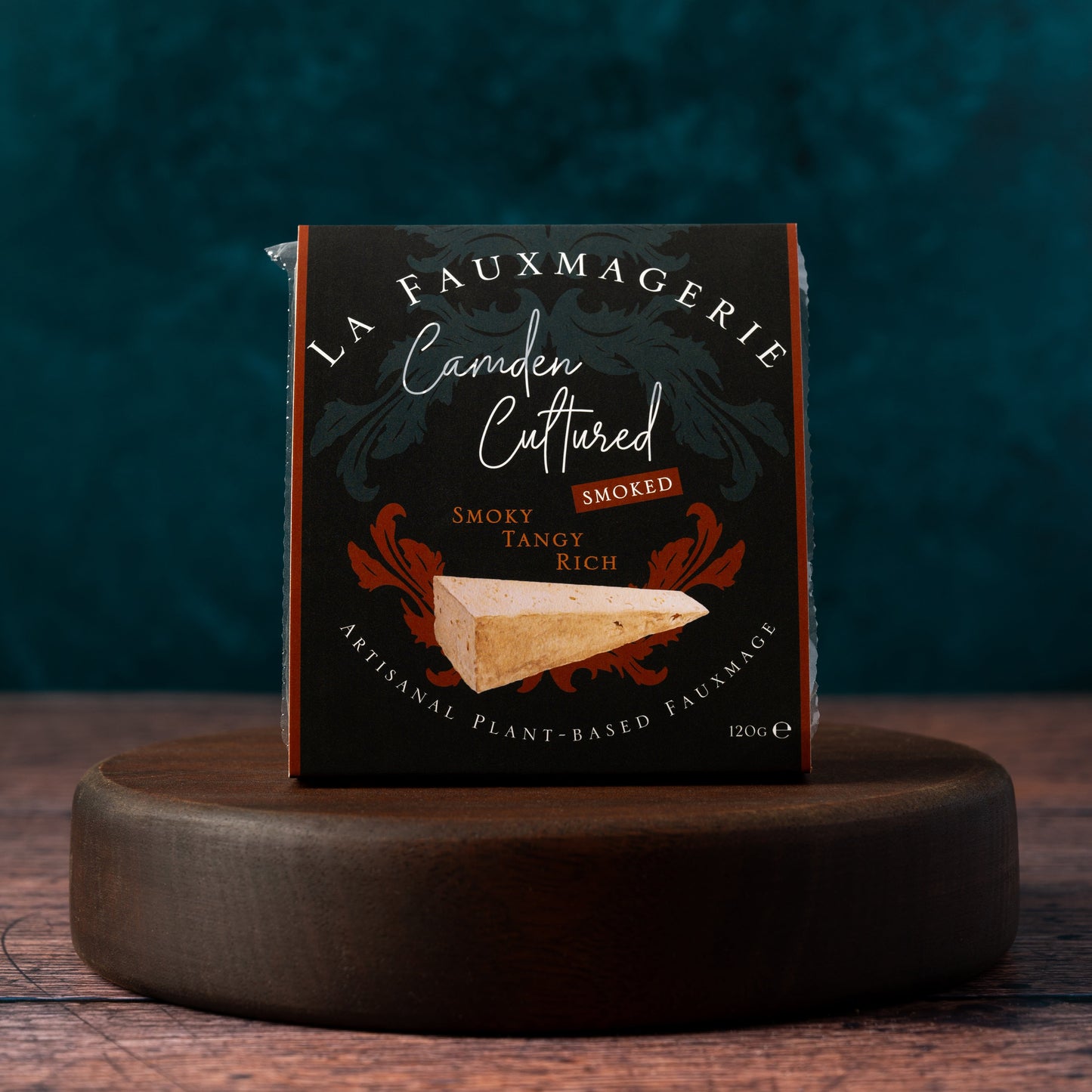 Box of La Fauxmagerie Camden Cultured smoked vegan cheese on a wooden stand with a dark background